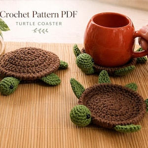 May include: Crochet turtle coasters in brown and green, with the text "Crochet Pattern PDF TURTLE COASTER". The coasters are handmade and feature a turtle design. A red mug sits on one of the coasters. The coasters are on a bamboo surface.