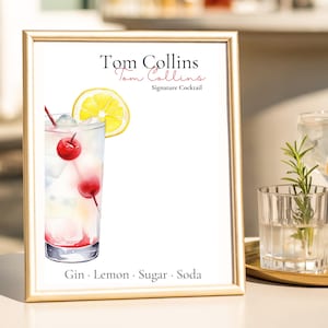 Può includere: Un cartello dorato con la scritta "Tom Collins" e un'illustrazione ad acquerello del cocktail. L'immagine include ciliegie, una fetta di limone e una cannuccia rossa. Gli ingredienti "Gin, Lemon, Sugar, Soda" sono elencati in basso.
