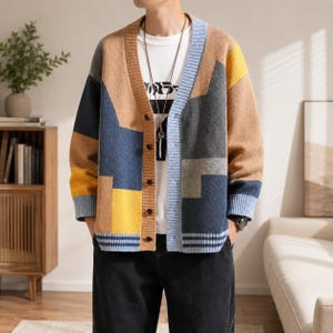 Puede incluir: Un cárdigan de manga larga con cuello en V que presenta un patrón de bloques de color en tonos beige, azul marino, gris y amarillo. La prenda de punto tiene cierre frontal de botones, puños acanalados y un dobladillo con rayas azules y beige.