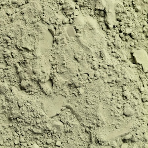May include: Close-up of a pile of fine, light green powder with a textured, granular appearance. The powder has a matte finish and appears to be a natural substance, possibly a cosmetic ingredient or a food additive. The image is well-lit, highlighting the texture.
