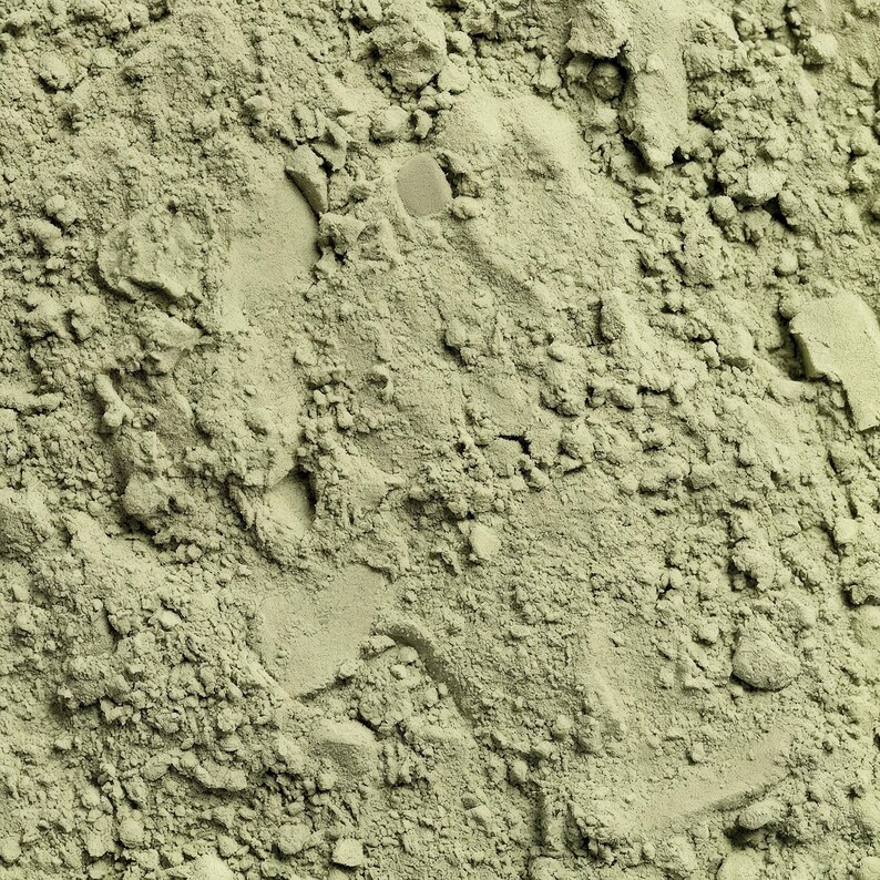 May include: Close-up of a pile of fine, light green powder with a textured, granular appearance. The powder has a matte finish and appears to be a natural substance, possibly a cosmetic ingredient or a food additive. The image is well-lit, highlighting the texture.