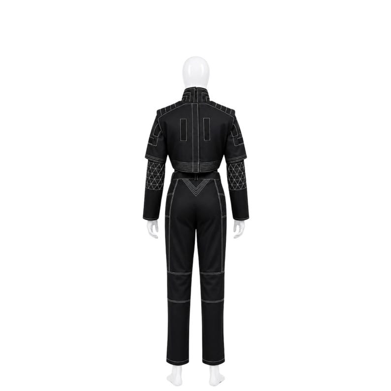 May include: Black jumpsuit with white stitching. The outfit features a cropped jacket with geometric patterns on the sleeves and shoulders, and matching trousers. The jumpsuit is displayed on a mannequin.