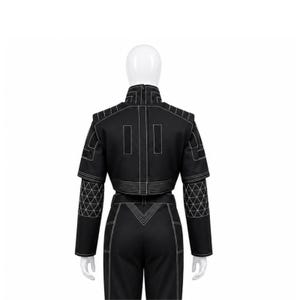 May include: Black two-piece outfit with white stitching. The cropped jacket features geometric patterns on the sleeves. The high-waisted trousers have a V-shaped design at the waist. The outfit is displayed on a mannequin.