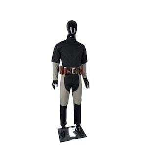 May include: A black and gray costume displayed on a mannequin. The outfit includes a short-sleeved top, pants, and a belt with pouches. The mannequin is black and stands on a black base. The costume has a futuristic or tactical design.