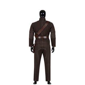 Puede incluir: Un disfraz marr&oacute;n exhibido en un maniqu&iacute; negro. El atuendo incluye una chaqueta, pantalones, cintur&oacute;n y una bandolera. La chaqueta tiene patrones geom&eacute;tricos en los hombros y los pantalones tienen costuras blancas.