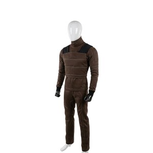 May include: A brown jumpsuit with a high collar, black shoulder accents, and white stitching. The long-sleeved top and pants are worn by a mannequin. Black gloves and white shoes complete the outfit.