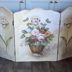 May include: A three-panel wooden screen with a floral design. The center panel features a basket of roses, hydrangeas, and other flowers. The side panels have a single tulip. The background is a light beige with a distressed look.