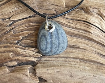 Può includere: Un ciondolo in pietra grigia con un anello d'argento e una collana in cordoncino di cuoio nero. La pietra ha un motivo naturale striato.