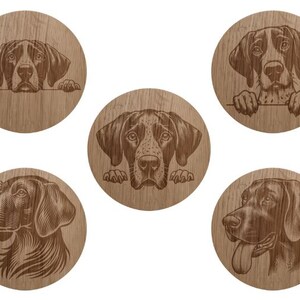 May include: Five circular wooden coasters, each featuring a detailed, dark brown engraved illustration of a dog's head. The designs include dogs peeking over an edge, a side profile, and a dog with its tongue out, all set against a wood grain.