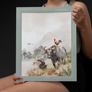 Puede incluir: Una impresión en acuarela enmarcada que presenta un toro con un gallo en su espalda y una serpiente en primer plano. La obra de arte tiene una paleta de colores apagados con un fondo de paisaje. El marco es de color verde claro.