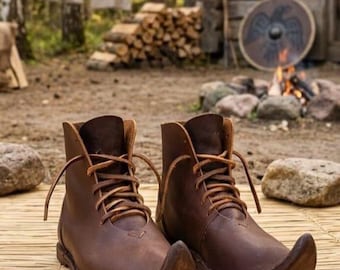 May include: A pair of brown leather boots with pointed toes and laced closures. The boots are made of a dark brown leather and have a vintage, rustic appearance. The boots are designed for historical reenactment or costume use.