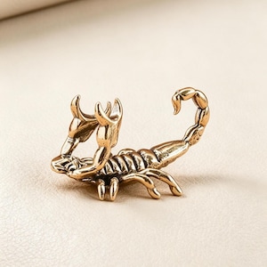 Könnte beinhalten: Detaillierte, goldfarbene Skorpionfigur. Der Skorpion ist mit erhobenen Scheren und nach oben gebogenem Schwanz dargestellt. Die Skulptur weist komplizierte Details auf, darunter ein segmentierter Körper und strukturierte Klauen. Das Gesamtdesign ist realistisch und künstlerisch.