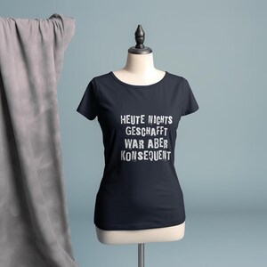 Könnte beinhalten: Marineblaues T-Shirt mit dem deutschen Text "HEUTE NICHTS GESCHAFFT WAR ABER KONSEQUENT" in Weiß, auf einer Schaufensterpuppe dargestellt. Das Shirt hat einen runden Ausschnitt und kurze Ärmel.