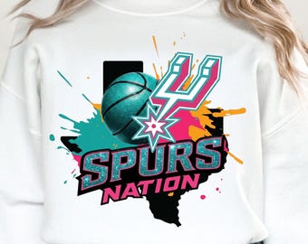 May include: White sweatshirt with a vibrant graphic. The design showcases a teal basketball, the Spurs logo, and the text "SPURS NATION" over a black outline of Texas. Teal, orange, and pink splashes enhance the design.