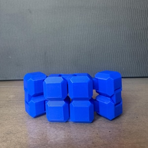 May include: A bright blue articulated fidget toy composed of multiple interconnected cube-shaped segments. The object features a geometric design with smooth, flat surfaces and visible hinge points that allow the structure to bend and fold.
