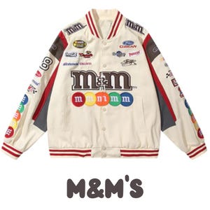 May include: Cream-coloured varsity jacket with the M&M's logo and colourful candy accents. Features patches and racing-style details. The jacket has a button-up front, red and white striped trim, and the text "M&M'S" at the bottom.
