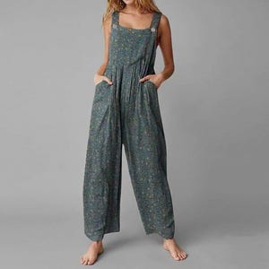 May include: A dark teal jumpsuit featuring a small-scale floral pattern in shades of yellow, orange, and light blue. The garment has wide shoulder straps, a square neckline, two side pockets, and a loose, relaxed fit with wide-leg trousers.
