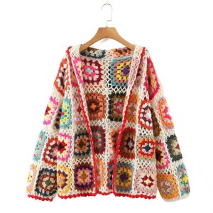 May include: A long-sleeved cardigan made of multi-coloured crochet granny squares in shades of pink, yellow, blue, orange, and purple. The garment features an open front design with a white crocheted lattice border and is displayed on a wooden hanger.