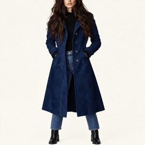 May include: A long, deep blue coat with a structured collar, long sleeves, and a button-front closure. The coat is worn over a black high-neck top, blue denim jeans, and black ankle boots. The coat features a tailored fit and side pockets.