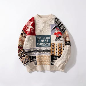 Puede incluir: Un suéter de manga larga con cuello redondo y diseño de parches con varios patrones de tejido. Incluye un panel rojo con copos de nieve blancos, un bloque azul con el texto "SKI CLUB T.W.97' VERMONT" y un oso bordado esquiando.