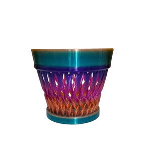 May include: A decorative, multi-colored planter with a woven design. The planter features a gradient of colors, including teal, purple, orange, and gold. The base and rim are teal, while the body transitions through the other colors. The planter is a unique home decor item.
