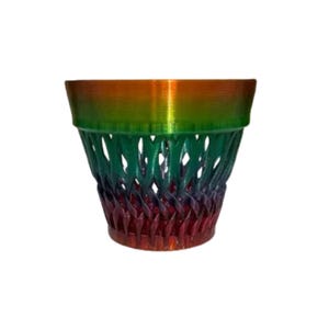 May include: A decorative planter with a woven design, featuring a gradient of colors. The top rim is orange, transitioning to green, and then to red at the base. The planter is suitable for indoor or outdoor use.