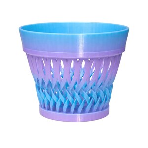 May include: A two-tone, 3D-printed planter in shades of blue and purple. The top rim is a solid light blue, transitioning to a woven pattern of blue and purple. The base is a solid purple.