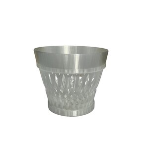May include: A clear, cylindrical container with a decorative, openwork design. The top and base are solid, while the body features a repeating pattern of curved lines. The container is made of a translucent material.