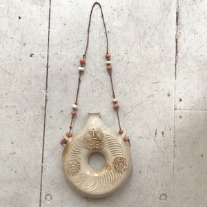 May include: A white ceramic bottle with a face and floral designs hanging from a brown leather cord with white and orange beads.