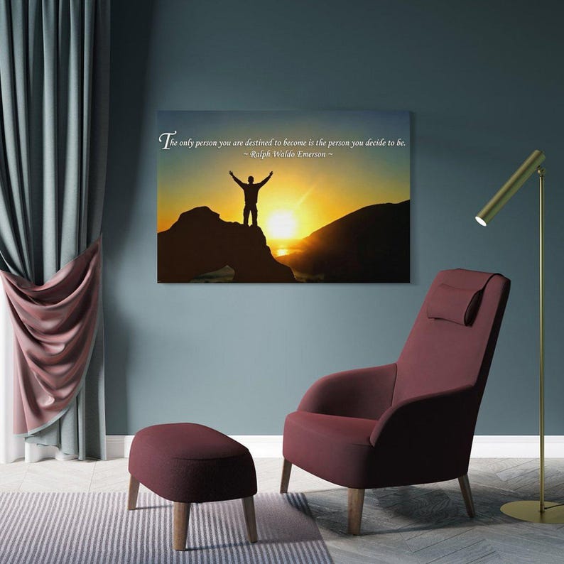 Pode incluir: Uma impress&atilde;o de arte de parede com uma cita&ccedil;&atilde;o inspiradora e uma imagem de um homem numa montanha ao p&ocirc;r do sol. O texto diz: "A &uacute;nica pessoa que voc&ecirc; est&aacute; destinado a se tornar &eacute; a pessoa que voc&ecirc; decide ser". Uma poltrona e um pufe bord&ocirc; s&atilde;o vis&iacute;veis.