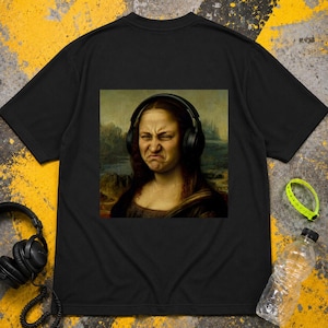 Könnte beinhalten: Ein schwarzes T-Shirt mit einem Grafikdruck einer Person mit verzerrtem Gesichtsausdruck, die einen schwarzen Over-Ear-Kopfhörer trägt. Das Kunstwerk ist vor einem gedämpften Landschaftshintergrund auf der Brust platziert.