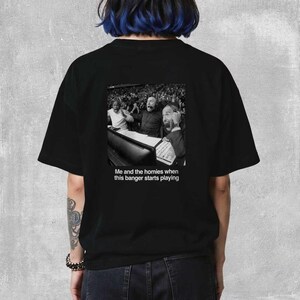 May include: Black t-shirt featuring a black and white image of people reacting with excitement. The text "Me and the homies when this banger starts playing" is below the image. The shirt is a casual, unisex style.
