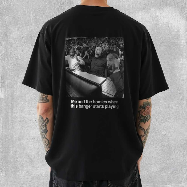 May include: Black t-shirt featuring a black and white image of three men reacting with excitement. The image is a meme with the text "Me and the homies when this banger starts playing". The shirt is a casual style.