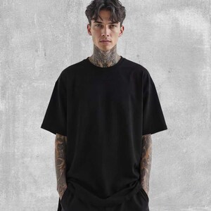 May include: A black oversized t-shirt with short sleeves. The shirt is made of a soft material and has a relaxed fit. The model is wearing the shirt and has tattoos on their arms and neck.