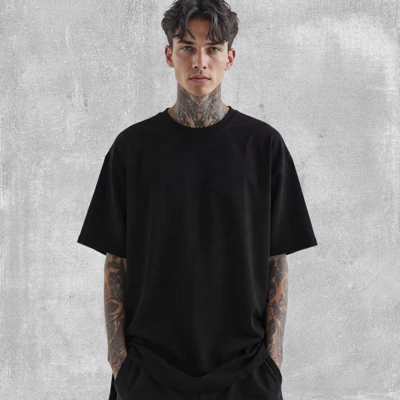 May include: A black oversized t-shirt with short sleeves. The shirt is made of a soft material and has a relaxed fit. The model is wearing the shirt and has tattoos on their arms and neck.