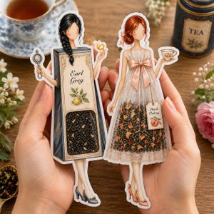 Può includere: Due adesivi fustellati con figure illustrate. Una figura ha i capelli neri e indossa un vestito a forma di scatola di tè Earl Grey con un limone. L'altra figura ha i capelli rossi e indossa un vestito di pizzo pieno di foglie di tè Peach Oolong.