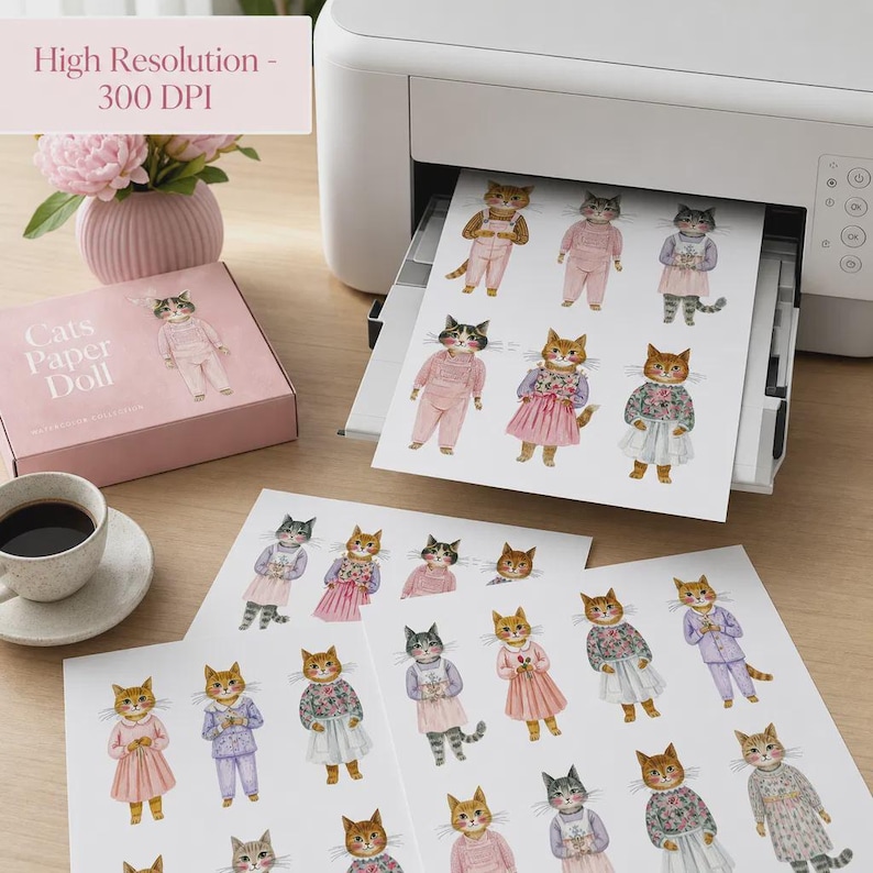 K&ouml;nnte beinhalten: Ein wei&szlig;er Drucker gibt ein Blatt Papier mit mehreren Aquarellillustrationen von Katzen in verschiedenen Outfits aus, neben einer rosa Schachtel mit der Aufschrift Cats Paper Doll und einer Vase mit rosa Blumen. Das Papier zeigt Katzen in Kleidern.