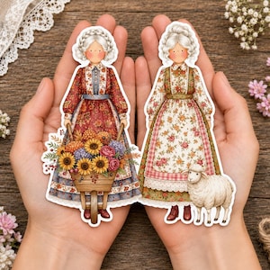 Könnte beinhalten: Zwei gestanzte Aufkleber mit Illustrationen von Figuren mit weißem geflochtenem Haar in Blumenkleidern. Eine Figur schiebt eine hölzerne Schubkarre voller Sonnenblumen und Rosen, während die andere neben einem kleinen weißen Schaf steht.