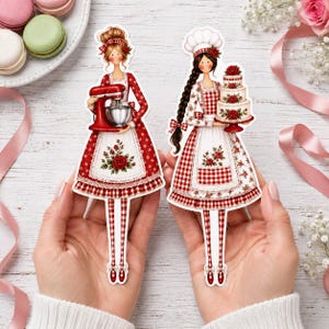 Può includere: Due illustrazioni in carta fustellata di pasticceri che indossano grembiuli a quadretti rossi e bianchi con accenti floreali. Un pasticcere tiene in mano una planetaria rossa, l'altro indossa un cappello da chef e regge una torta a tre piani.