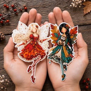 May include: Two die-cut stickers featuring fairy illustrations. The left fairy has blonde hair, a red dress with autumn leaves, and white wings. The right fairy has black hair, a teal dress, autumn leaf wings, and holds a small brown owl.