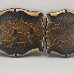 May include: Two rectangular light switch plates with a dark bronze finish and a textured, cracked surface pattern. The larger plate features three toggle switch openings, while the smaller plate has two toggle switch openings, both with smooth edges.