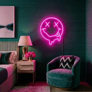 May include: A bright pink neon sign shaped like a melting smiley face with X-shaped eyes and a tongue sticking out. The circular light fixture features a glowing outline and a dripping effect at the bottom, mounted on a dark green textured wall.