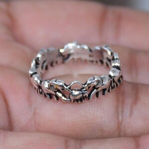 Könnte beinhalten: Ein Ring aus silberfarbenem Metall mit einem durchgehenden Banddesign, das aus mehreren kleinen, stilisierten Elefantenfiguren besteht, die in einem sich wiederholenden Muster um den gesamten Umfang des Rings angeordnet sind.