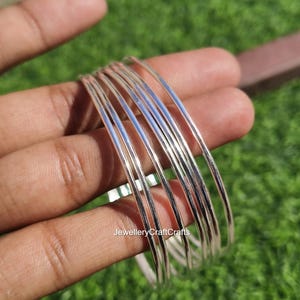 Peut inclure: Un ensemble de bracelets fins en argent. Les bracelets sont lisses et r&eacute;fl&eacute;chissants, avec un &eacute;clat m&eacute;tallique brillant. Les bijoux sont tenus dans une main sur fond d'herbe verte.