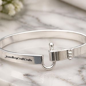Könnte beinhalten: Ein silbernes Armband mit Hakenverschluss. Auf dem Armband steht "JewelleryCraftCrafts". Das Schmuckstück wird auf einer Marmoroberfläche präsentiert. Der Umfang beträgt ca. 18 cm.