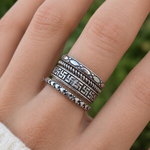 Könnte beinhalten: Nahaufnahme einer Hand mit fünf silbernen Ringen. Die Ringe weisen verschiedene Designs auf, darunter Herzen, geometrische Muster und Perlenstrukturen. Die Ringe sind auf einem Finger gestapelt und zeigen die verschiedenen Stile und Texturen.