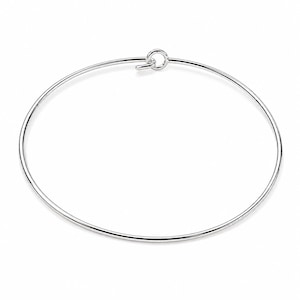 Peut inclure: Un bracelet jonc circulaire et fin en argent avec une finition métallique polie. Le bracelet présente un mécanisme de fermeture simple de type crochet et boucle sur le dessus, où une extrémité du fil forme une petite boucle et l'autre s'y accroche.