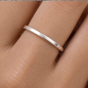 Könnte beinhalten: Ein minimalistischer Silberring wird an einem Finger getragen. Der Ring ist ein dünnes Band mit flacher Oberfläche. Der Hautton ist hell, und der Nagellack ist neutral. Der Ring ist ein schlichtes, elegantes Schmuckstück.