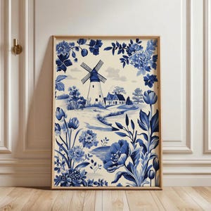 Könnte beinhalten: Gerahmtes Wandbild mit einer blau-weißen ländlichen Szene mit Windmühle, Haus und floralem Rand. Das Kunstwerk befindet sich in einem Holzrahmen und zeigt ein klassisches Toile-Design.