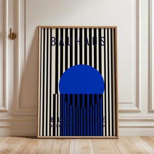 May include: Framed Bauhaus art print featuring a bold blue circle and vertical black and white stripes. The word "BAUHAUS" is at the top, with "BLUE LINES" and the date "1923" at the bottom. The artwork is in a wooden frame.